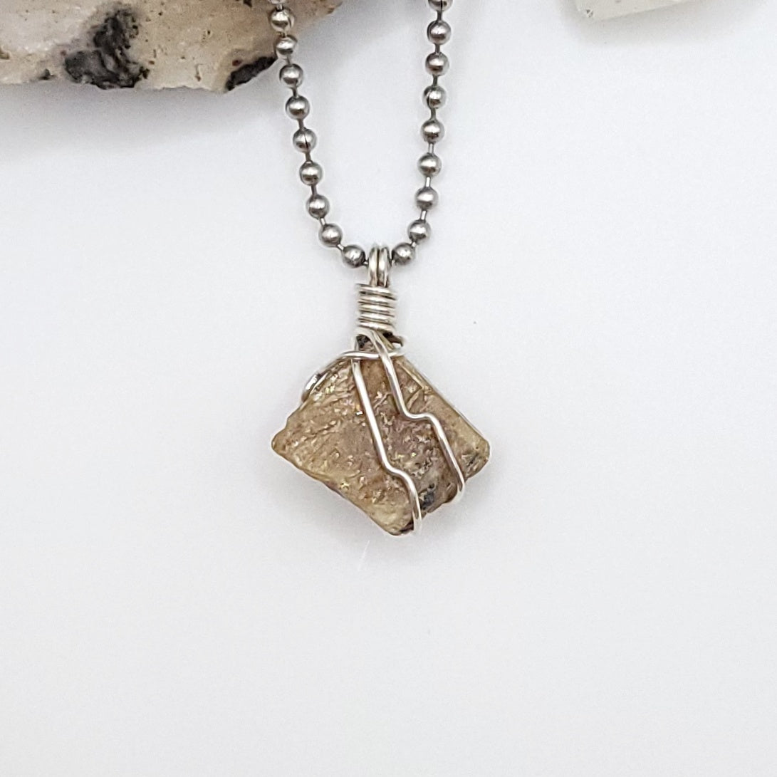 A honey yellow kyanite necklace wrapped in silver wire, suspended from a silver ball chain.