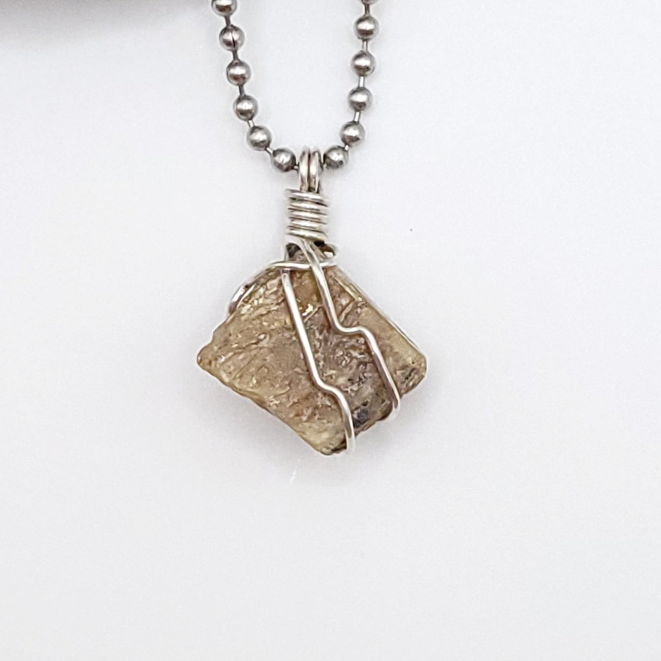 A honey yellow kyanite necklace wrapped in silver wire, suspended from a silver ball chain up close