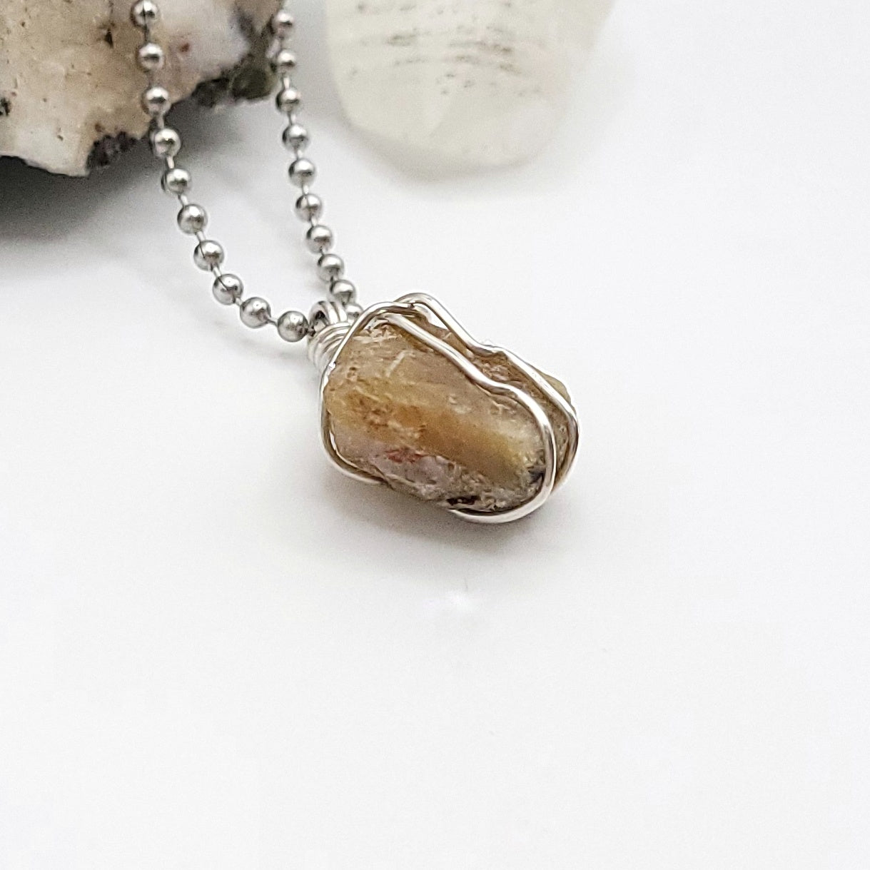 A honey yellow kyanite necklace wrapped in silver wire, suspended from a silver ball chain side view