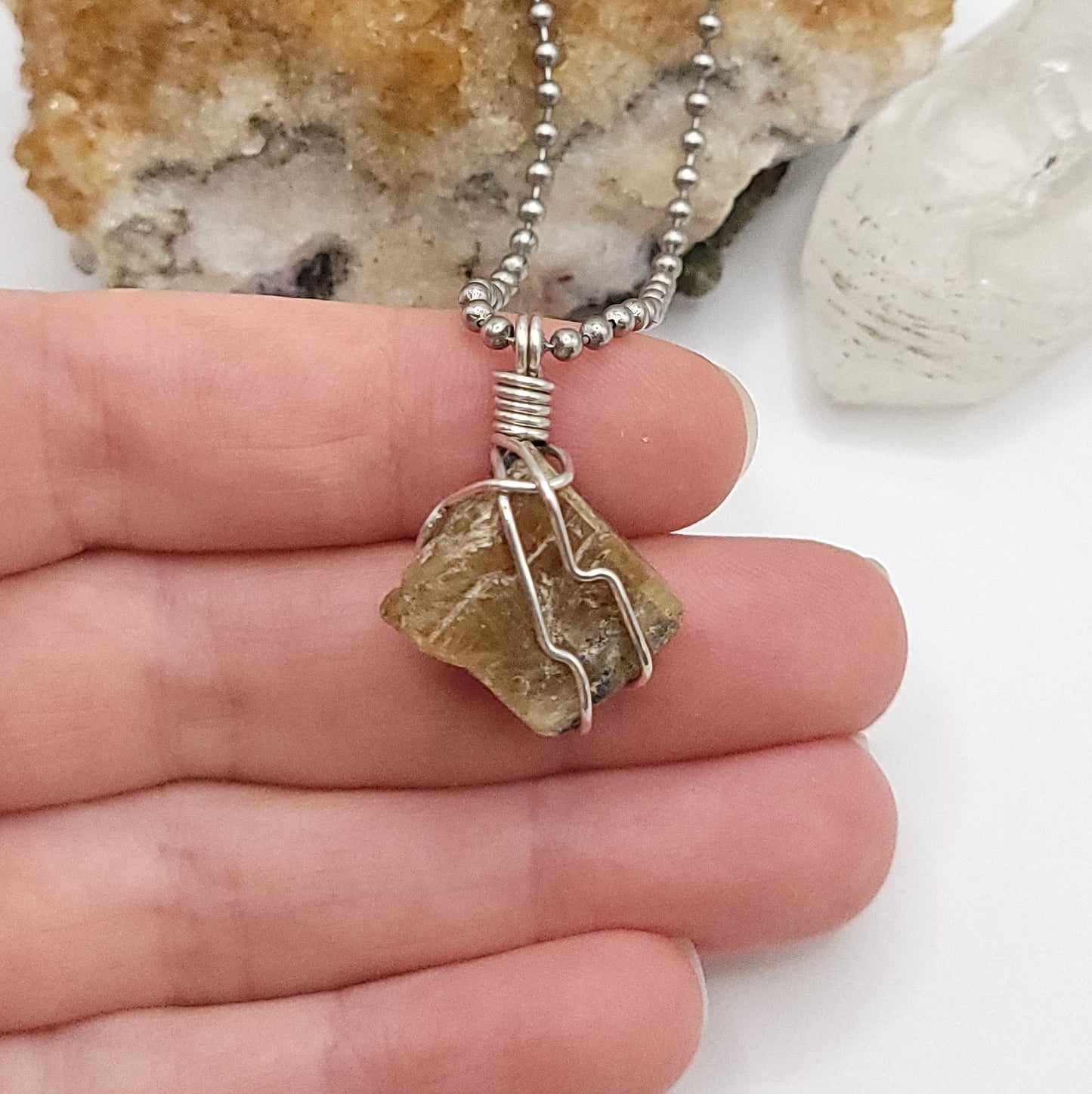 A honey yellow kyanite necklace wrapped in silver wire, suspended from a silver ball chain in hand