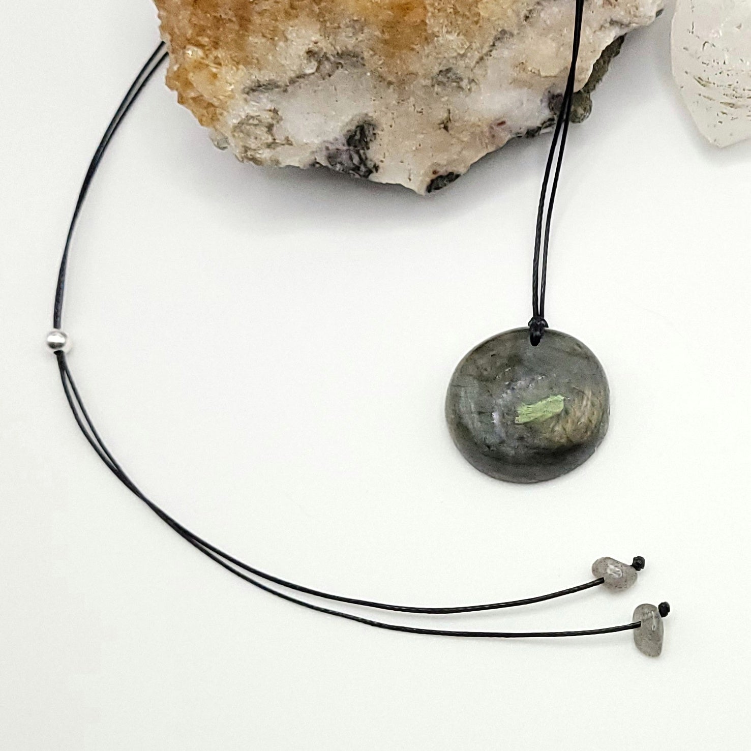 An adjustable Labradorite crystal necklace with a black waxed cotton cord, a sterling silver sliding bead, and a second crystal bead.