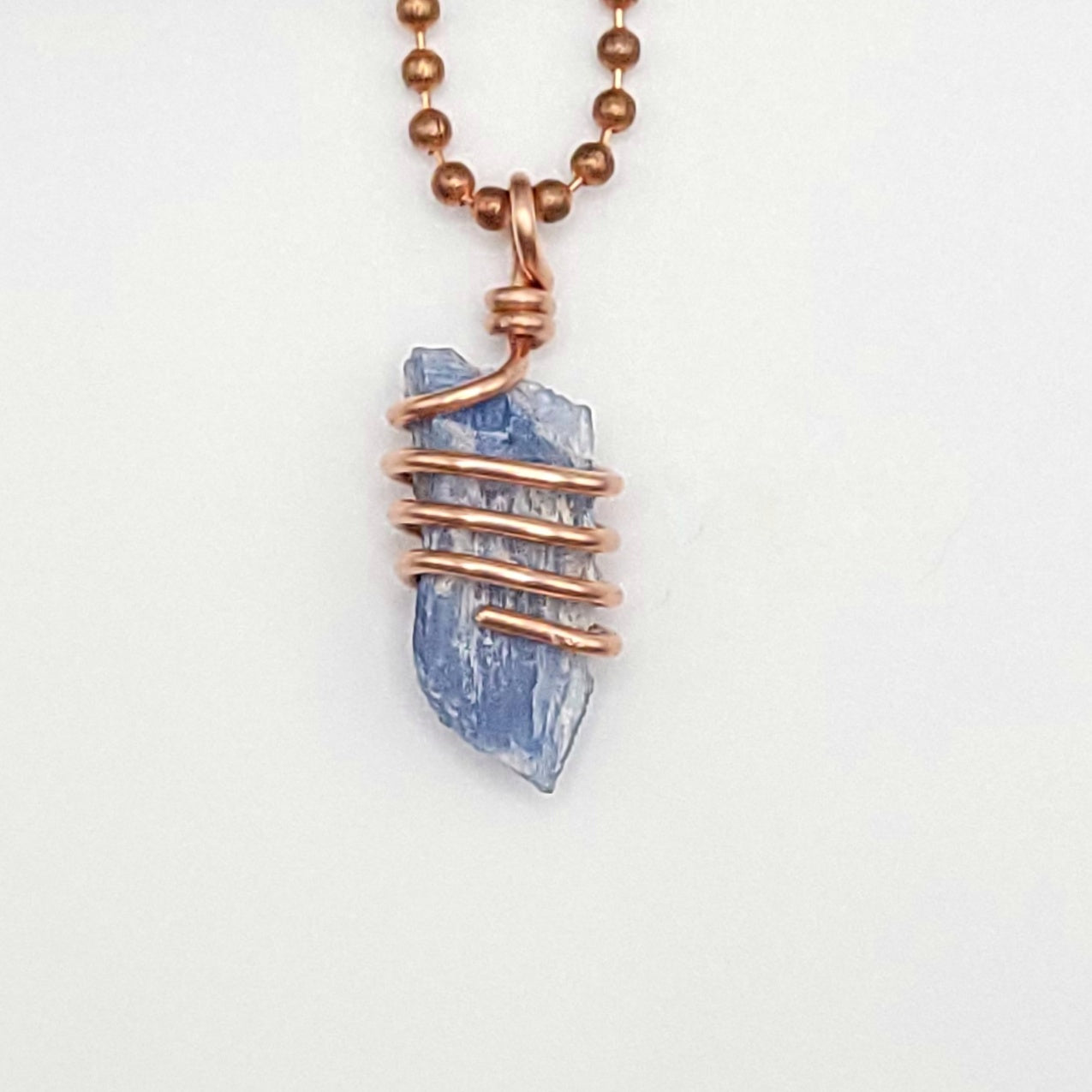 A raw Blue Kyanite crystal wrapped in copper wire, with a copper ball chain for a necklace close up