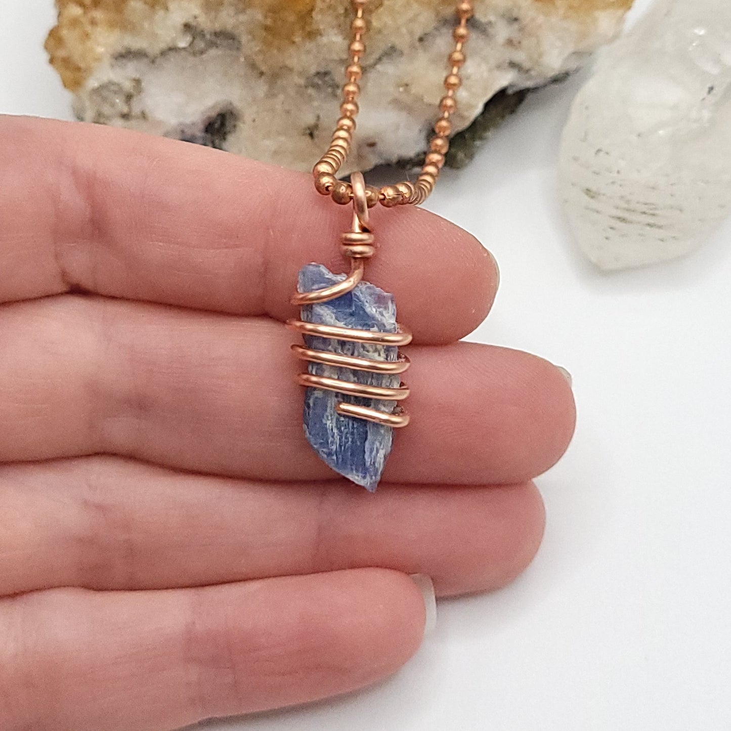 A raw Blue Kyanite crystal wrapped in copper wire, with a copper ball chain for a necklace in hand