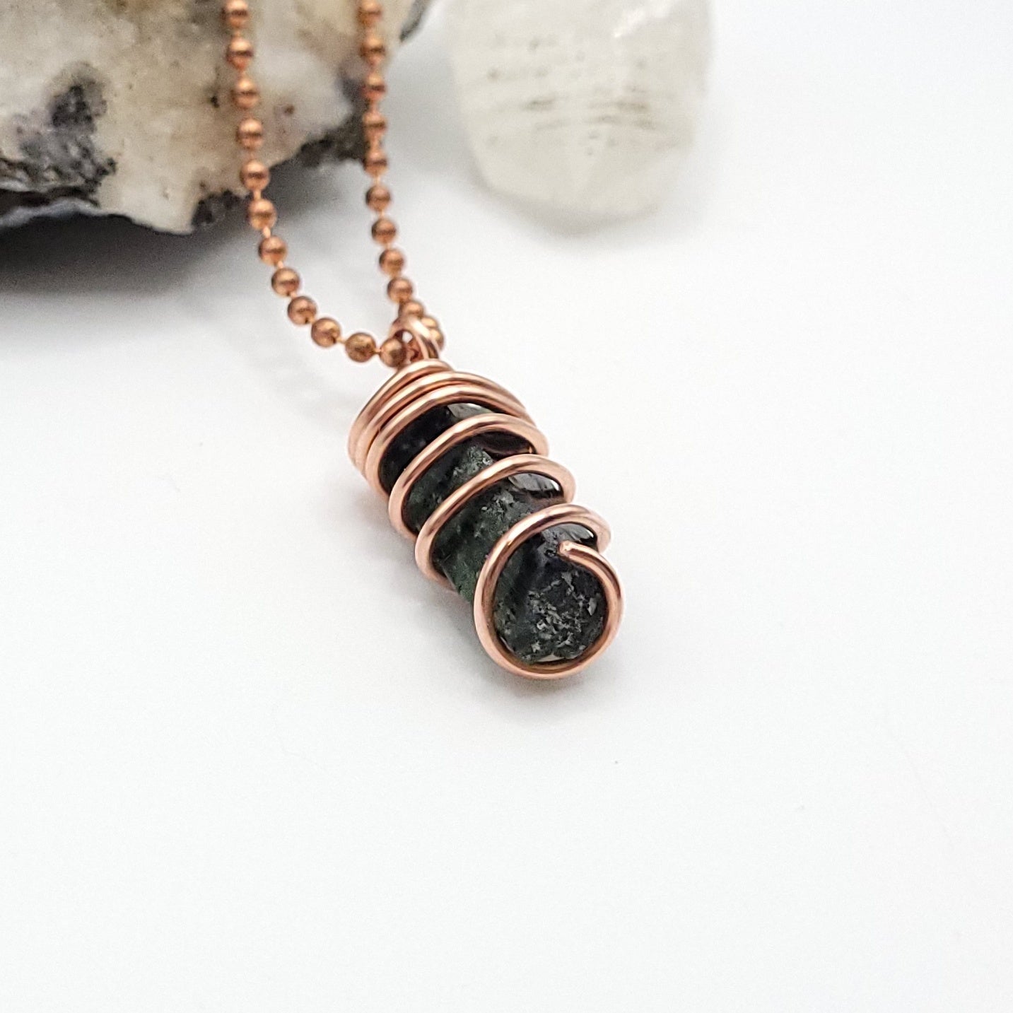 A raw Diopside crystal wrapped in copper wire with a copper ball chain side view