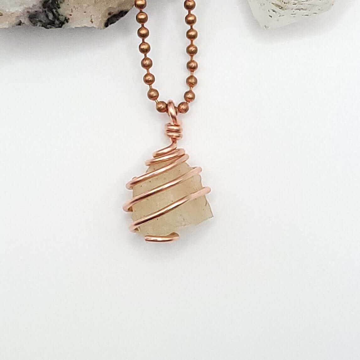 A necklace featuring a copper-wrapped raw Libyan Desert Glass crystal pendant on a copper ball chain.