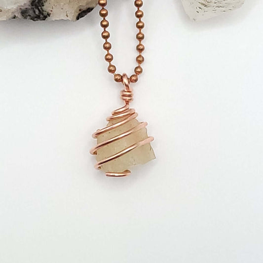 A necklace featuring a copper-wrapped raw Libyan Desert Glass crystal pendant on a copper ball chain.