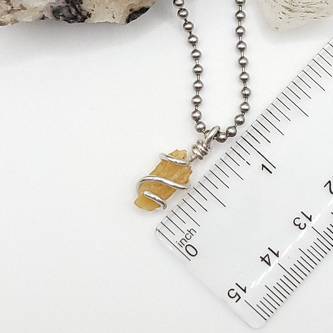 A honey yellow kyanite necklace wrapped in silver wire, suspended from a silver ball chain necklace measurement just under 1 inch