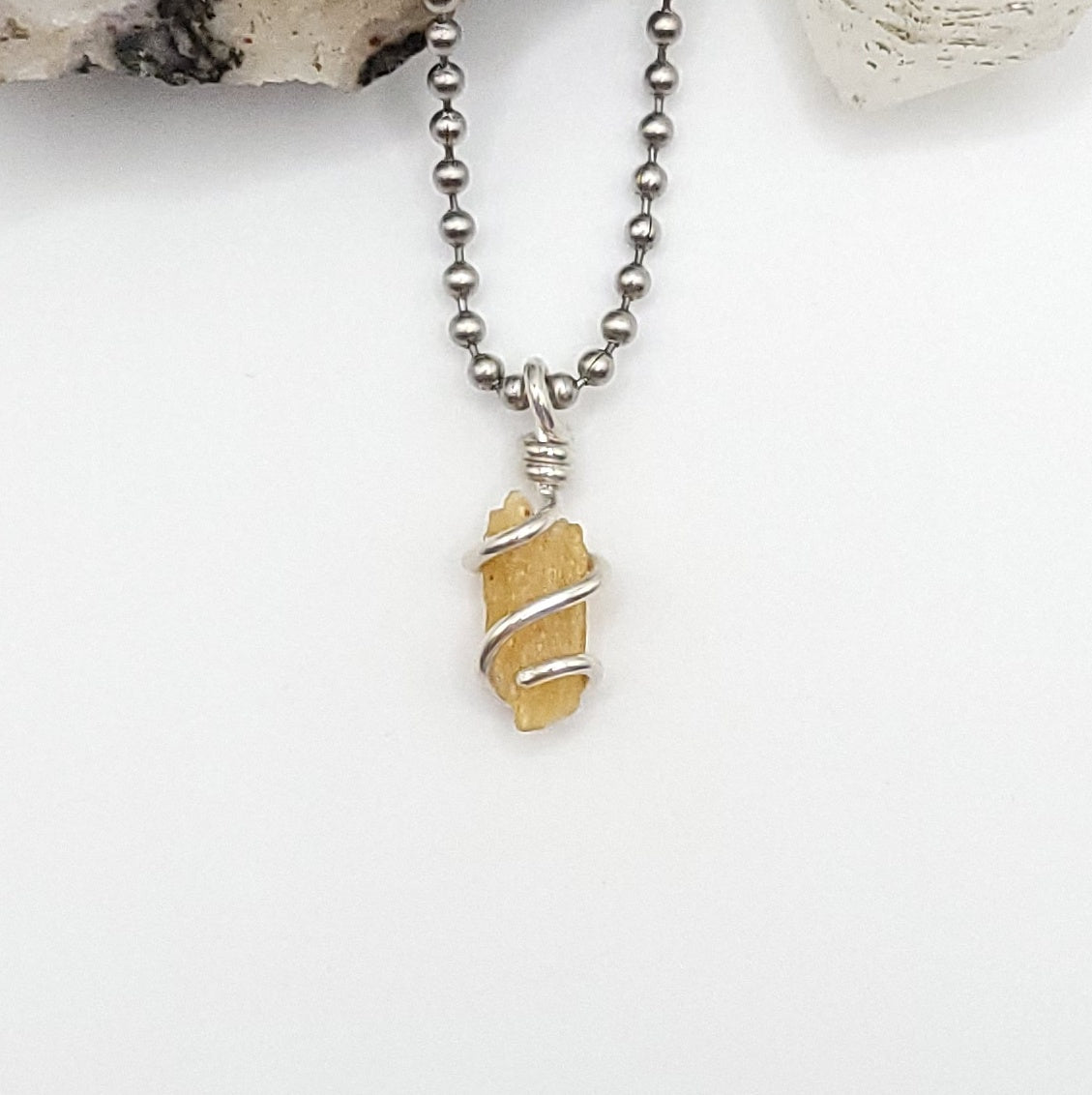 A honey yellow kyanite necklace wrapped in silver wire, suspended from a silver ball chain necklace.