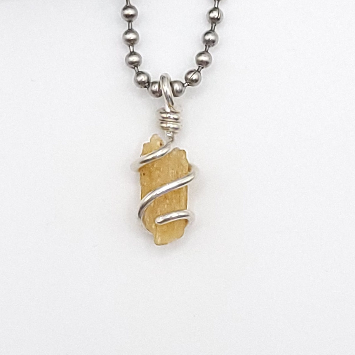 A honey yellow kyanite necklace wrapped in silver wire, suspended from a silver ball chain necklace up close