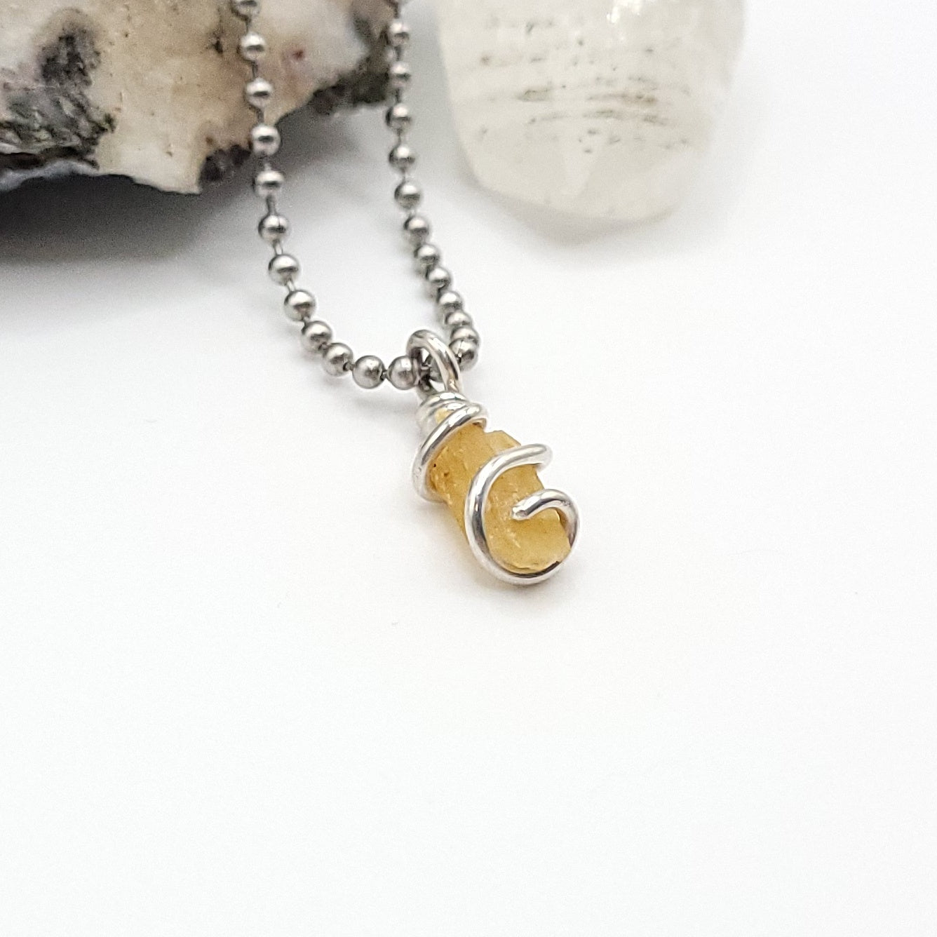 A honey yellow kyanite necklace wrapped in silver wire, suspended from a silver ball chain necklace side view