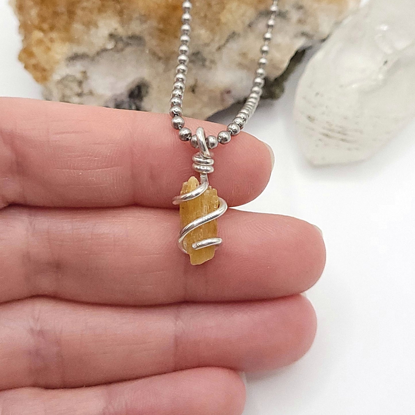 A honey yellow kyanite necklace wrapped in silver wire, suspended from a silver ball chain necklace in hand