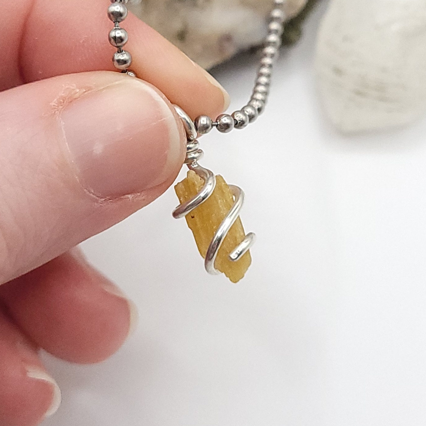 A honey yellow kyanite necklace wrapped in silver wire, suspended from a silver ball chain necklace up close in hand