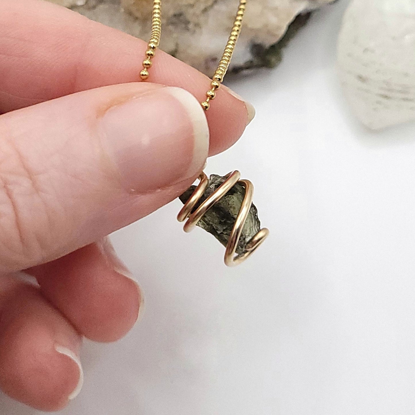 Raw Moldavite Necklace in Gold close up with white background and light behind it