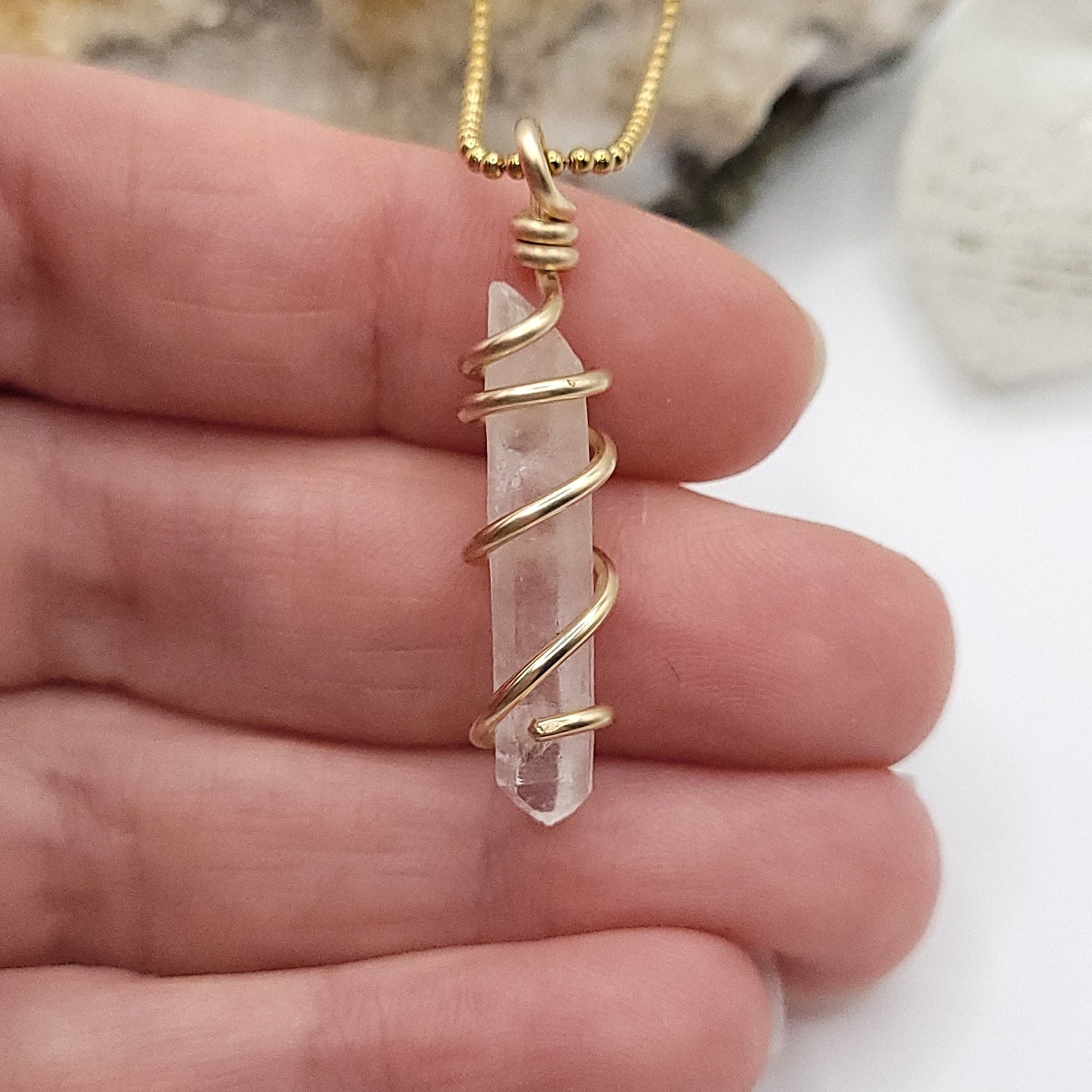 clear quartz necklace in gold close up in hand