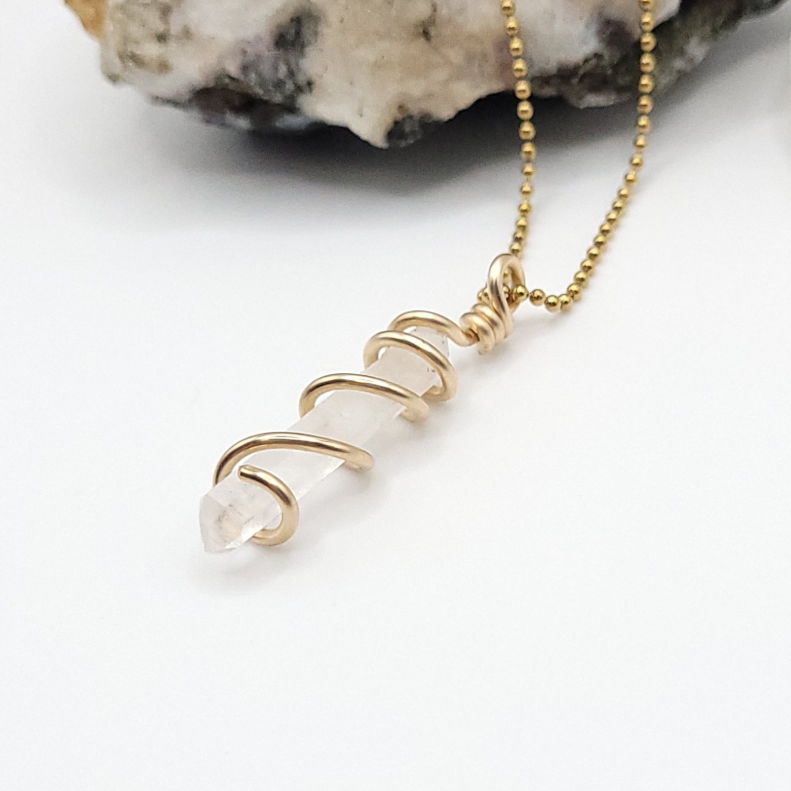 clear quartz necklace in gold side view on white background
