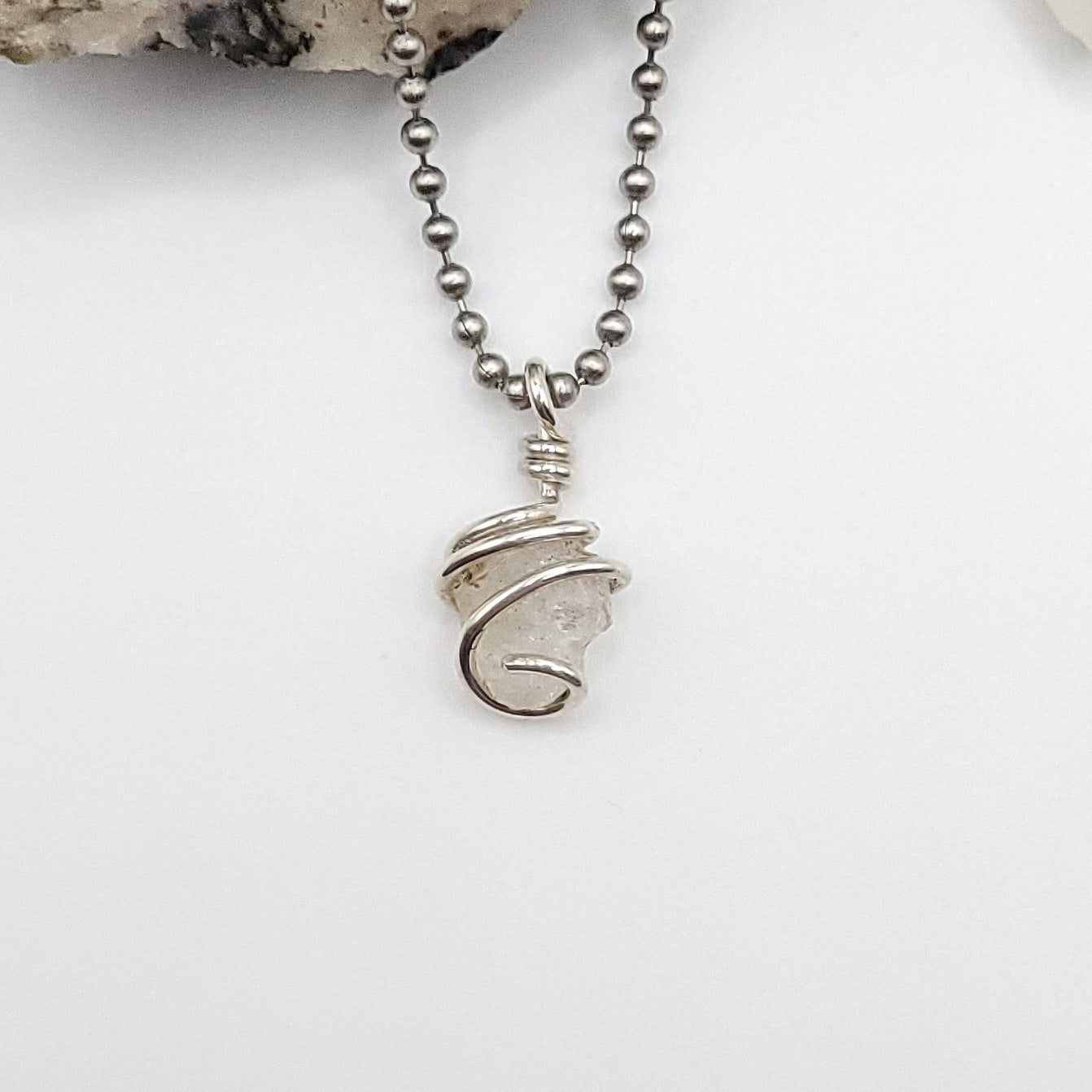 raw phenakite pendant in silver against white background