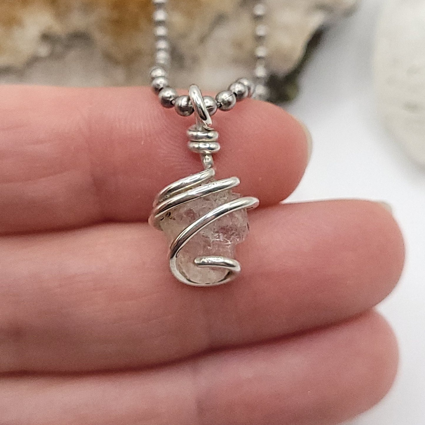 raw phenakite pendant in silver in hand close up