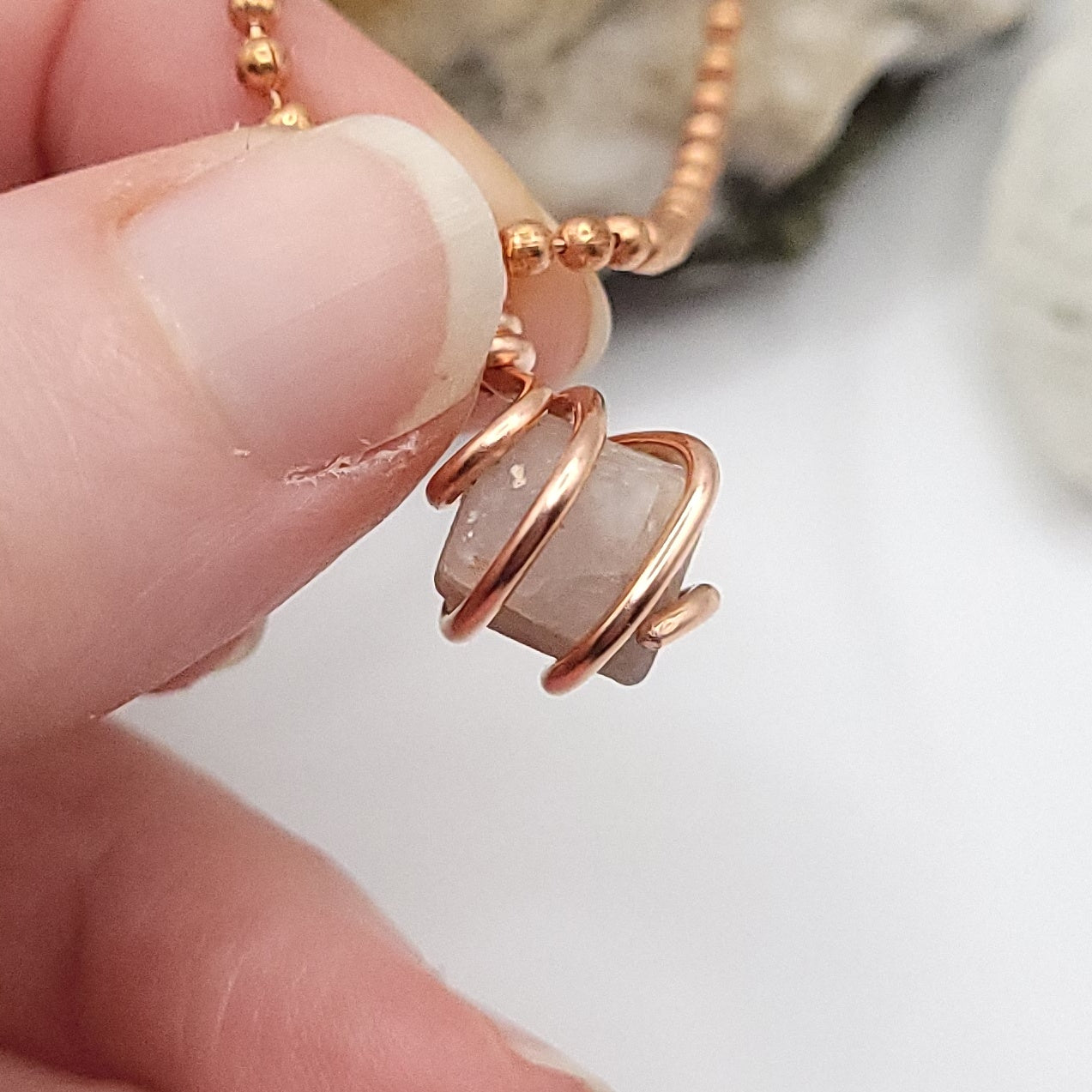 Hand holding a raw Beta Quartz necklace wrapped in copper wire, symbolizing transformation and energy flow.