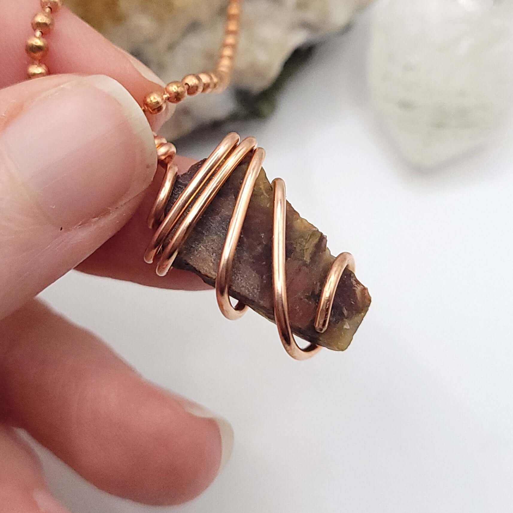 Hand holding a raw Pietersite necklace wrapped in copper wire, showcasing its natural beauty and energy.