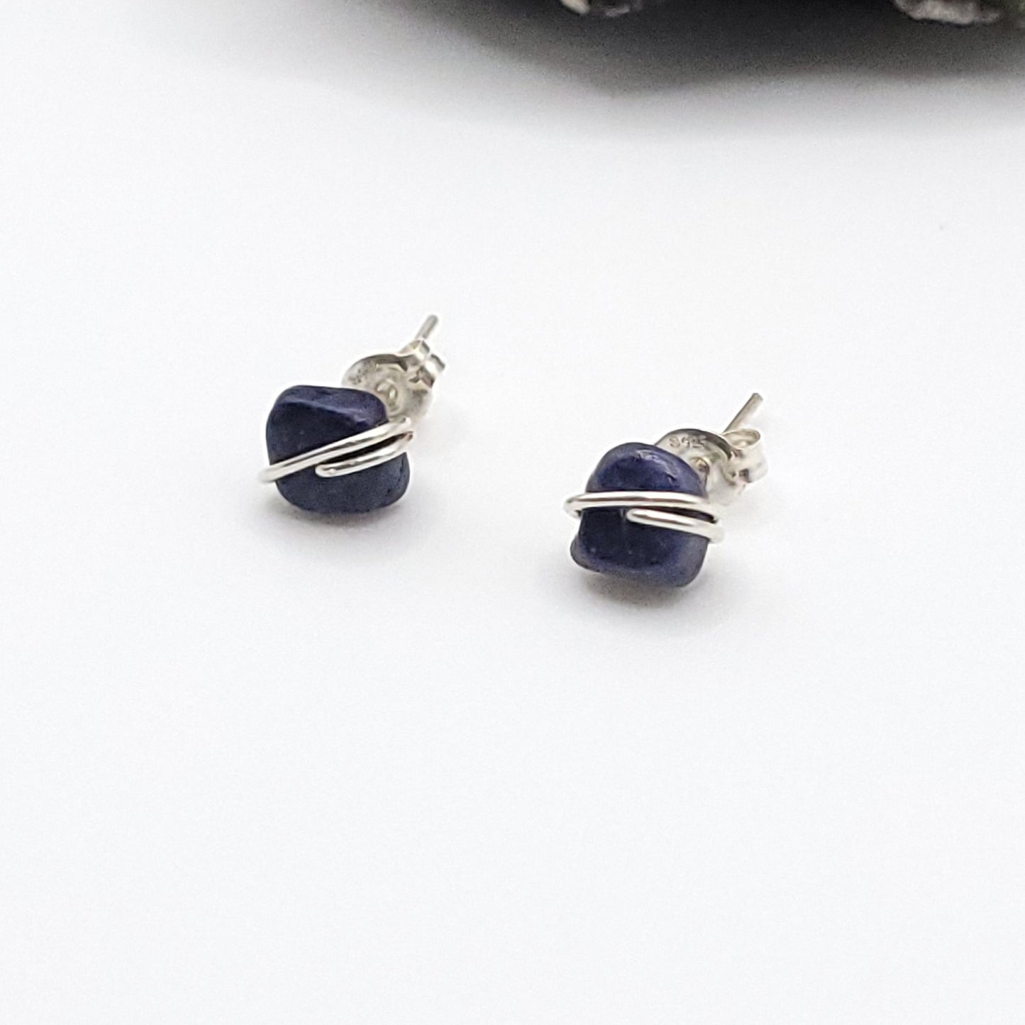 Pair of blue sapphire earrings with silver wire wrapping on a white background side view