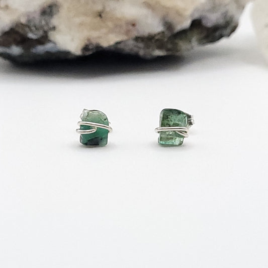 emerald stud earrings on a white background with a stone in the background