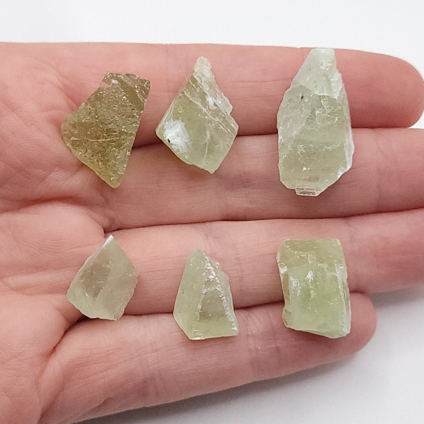 Raw green calcite necklace crystals displayed on a hand, showcasing the unique textures and colors of the stones.