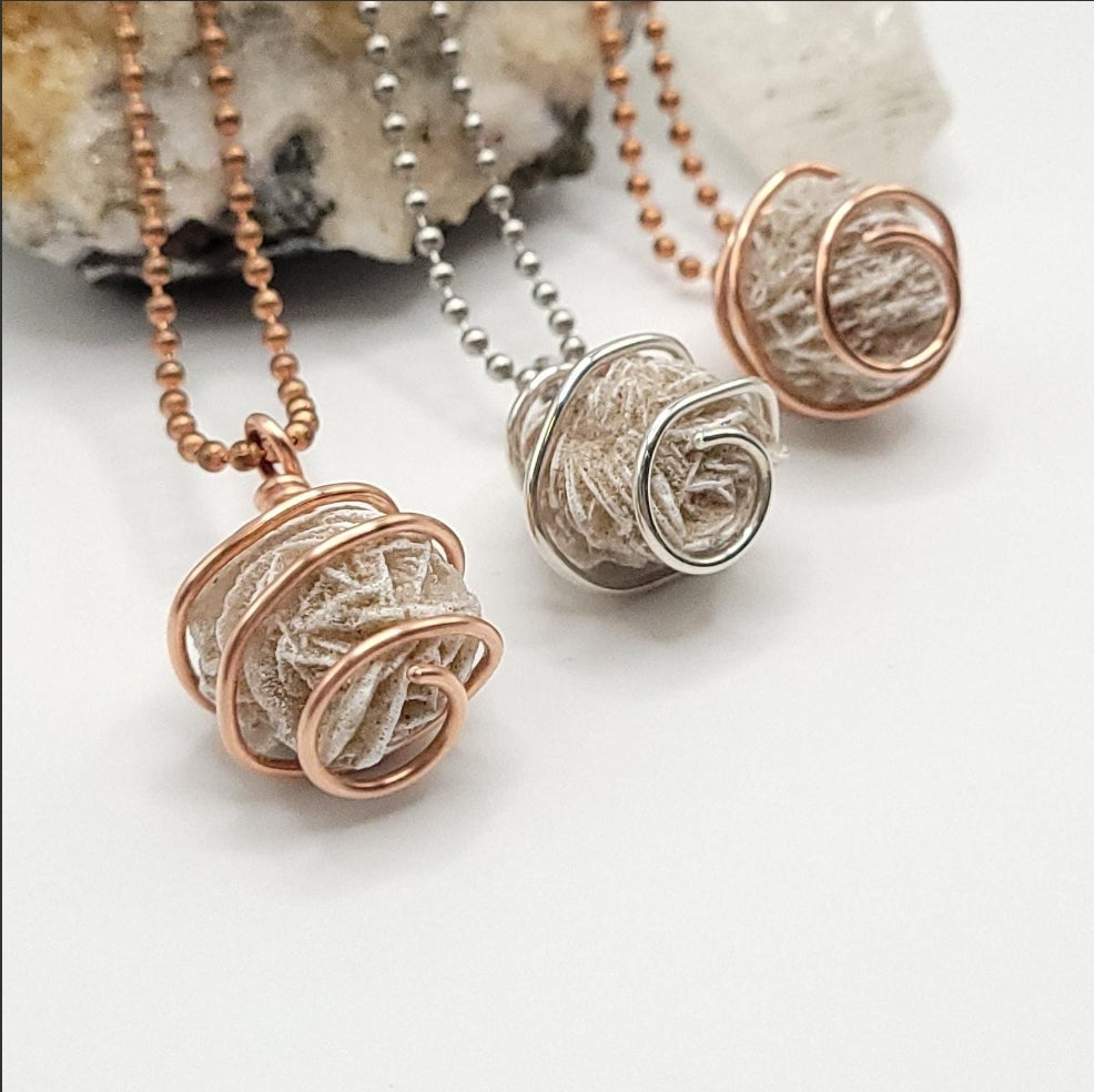three Silver and copper wire-wrapped desert rose selenite pendant necklaces on a white background