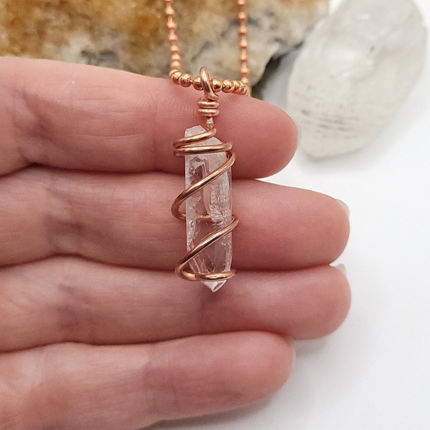 raw danburite pendant in copper wire in hand