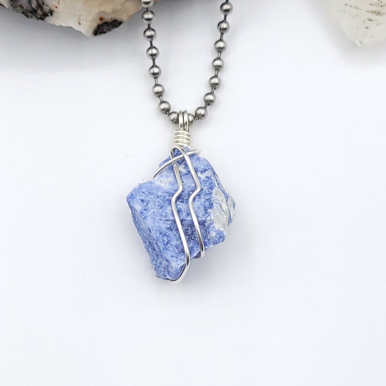 A sodalite crystal wrapped in silver wire with a stainless-steel ball chain close up