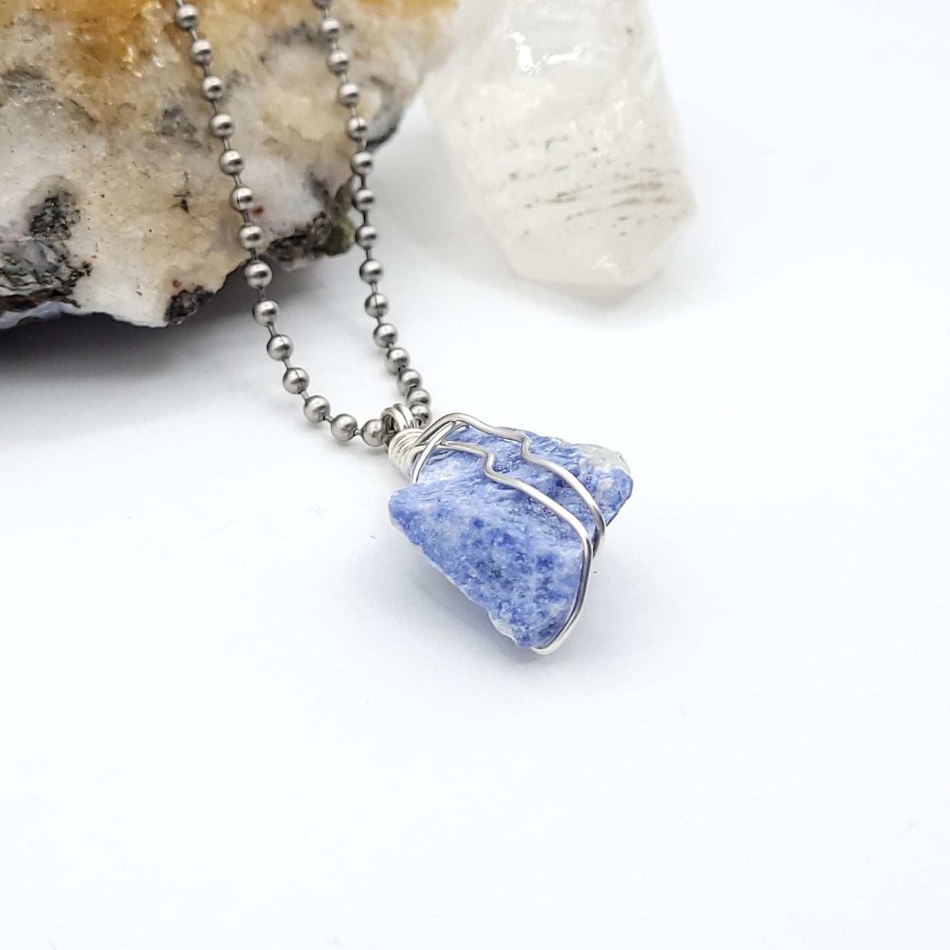 A sodalite crystal wrapped in silver wire with a stainless-steel ball chain side view