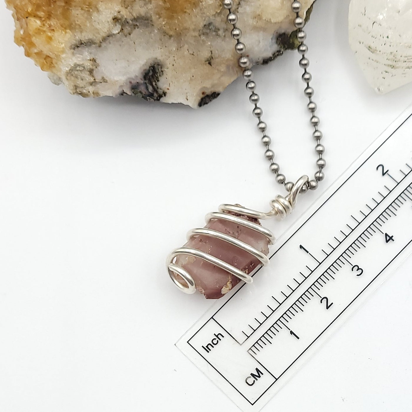 lithium quartz necklace in sterling silver wire on white background next to rule measuring about 1.5 inches