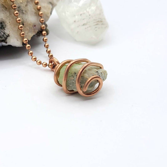 raw peridot wrapped in copper wire on a white background side view