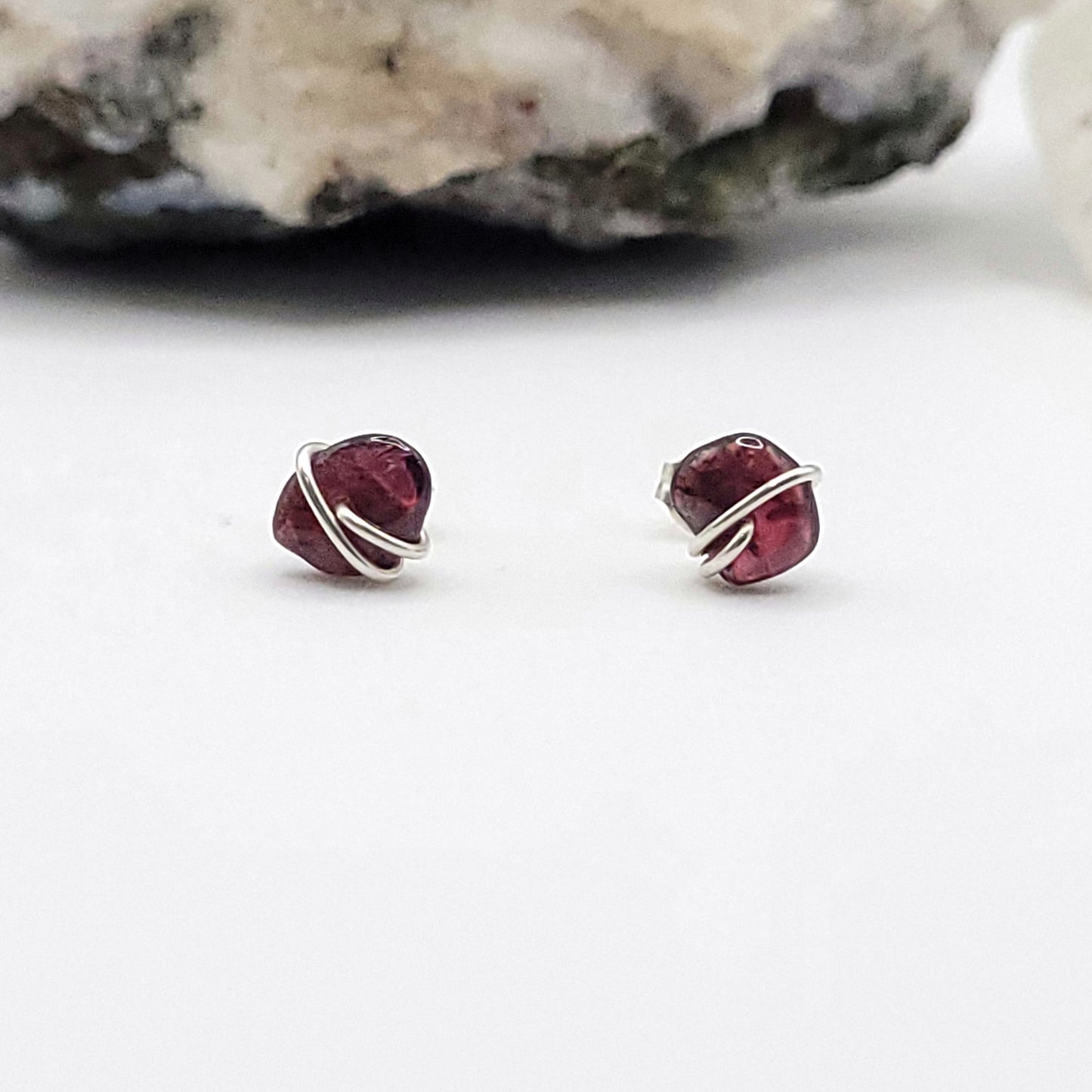 Pair of garnet stud earrings with silver wire wrapping on a white background.