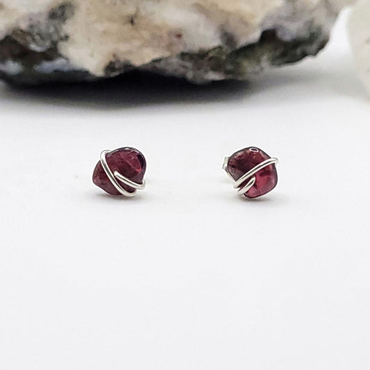 Pair of garnet stud earrings with silver wire wrapping on a white background.