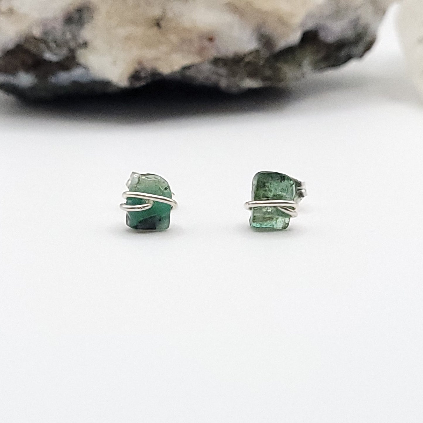 emerald stud earrings on a white background with a stone in the background
