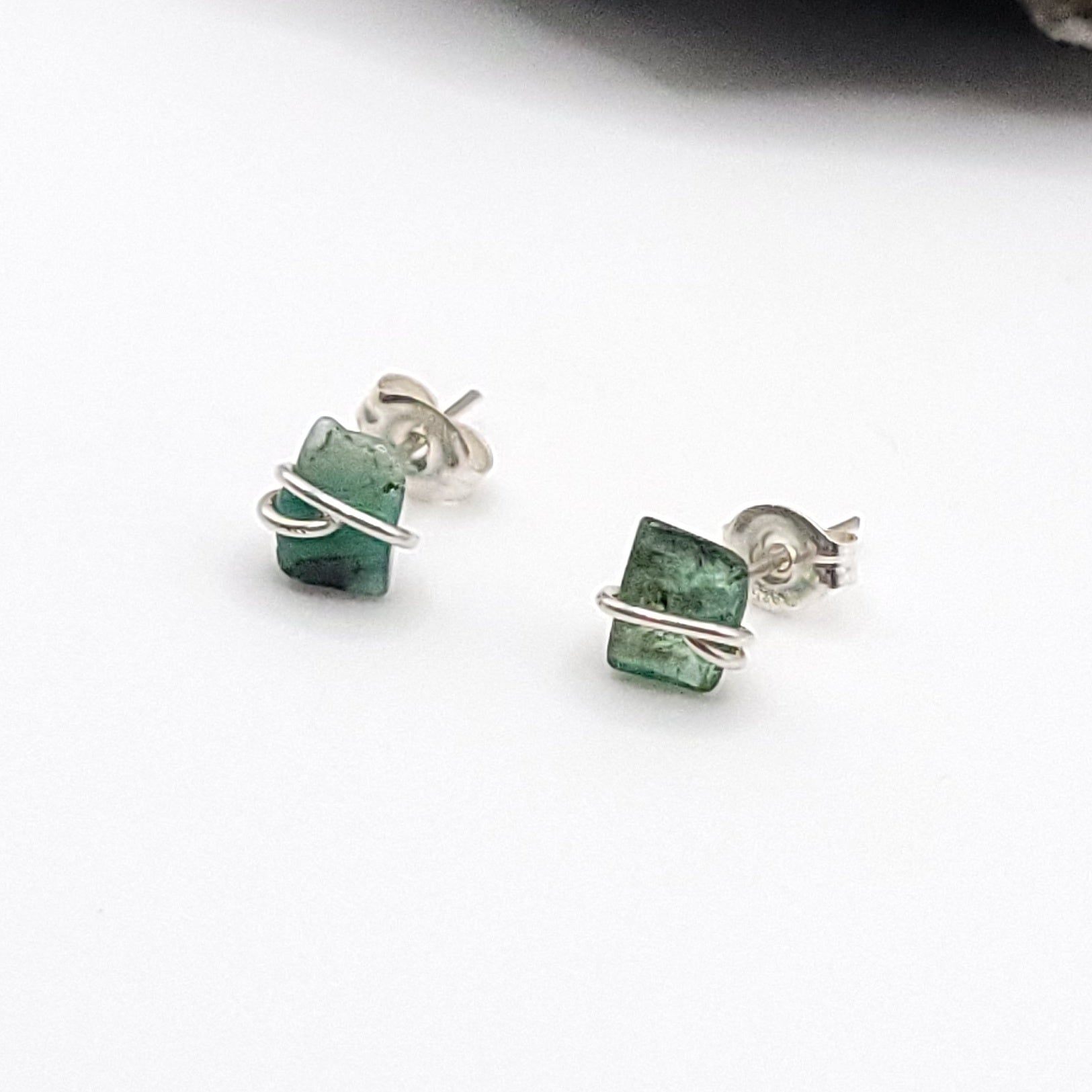 emerald stud earrings with silver wire wrapping on a white background