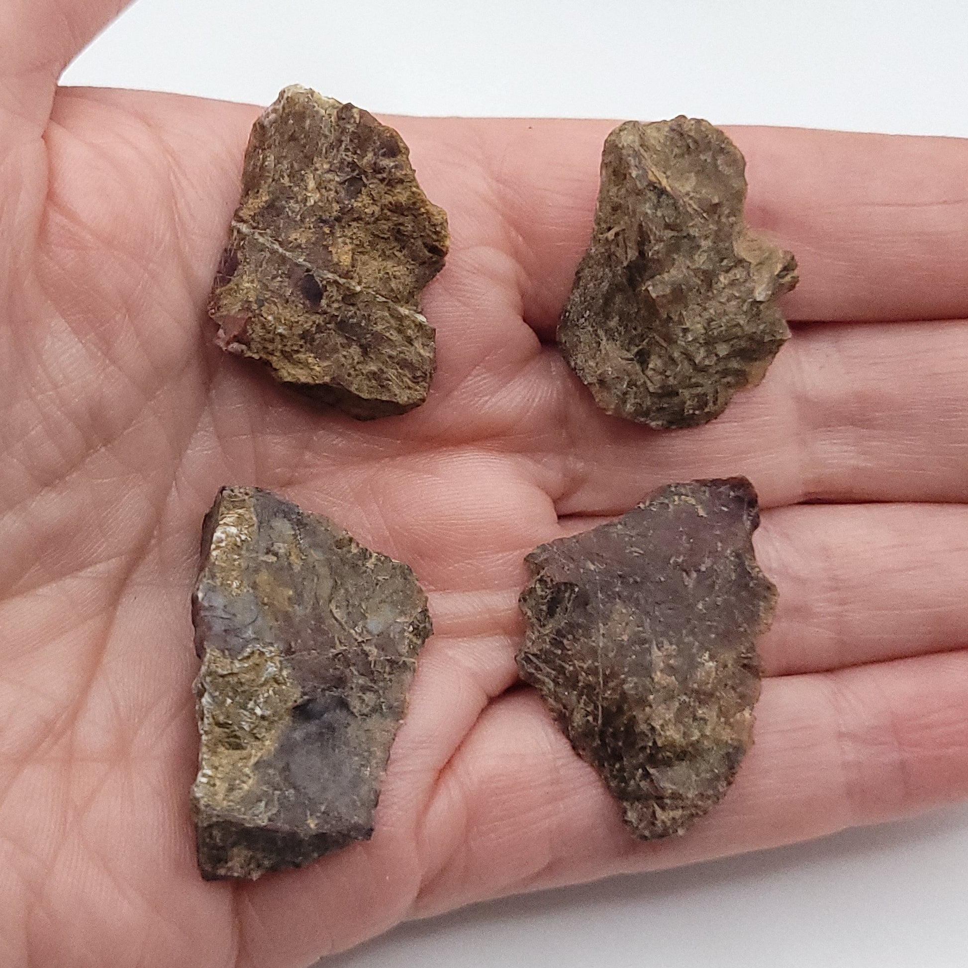 Natural raw Pietersite stones displayed on a hand, showcasing their unique textures and colors.