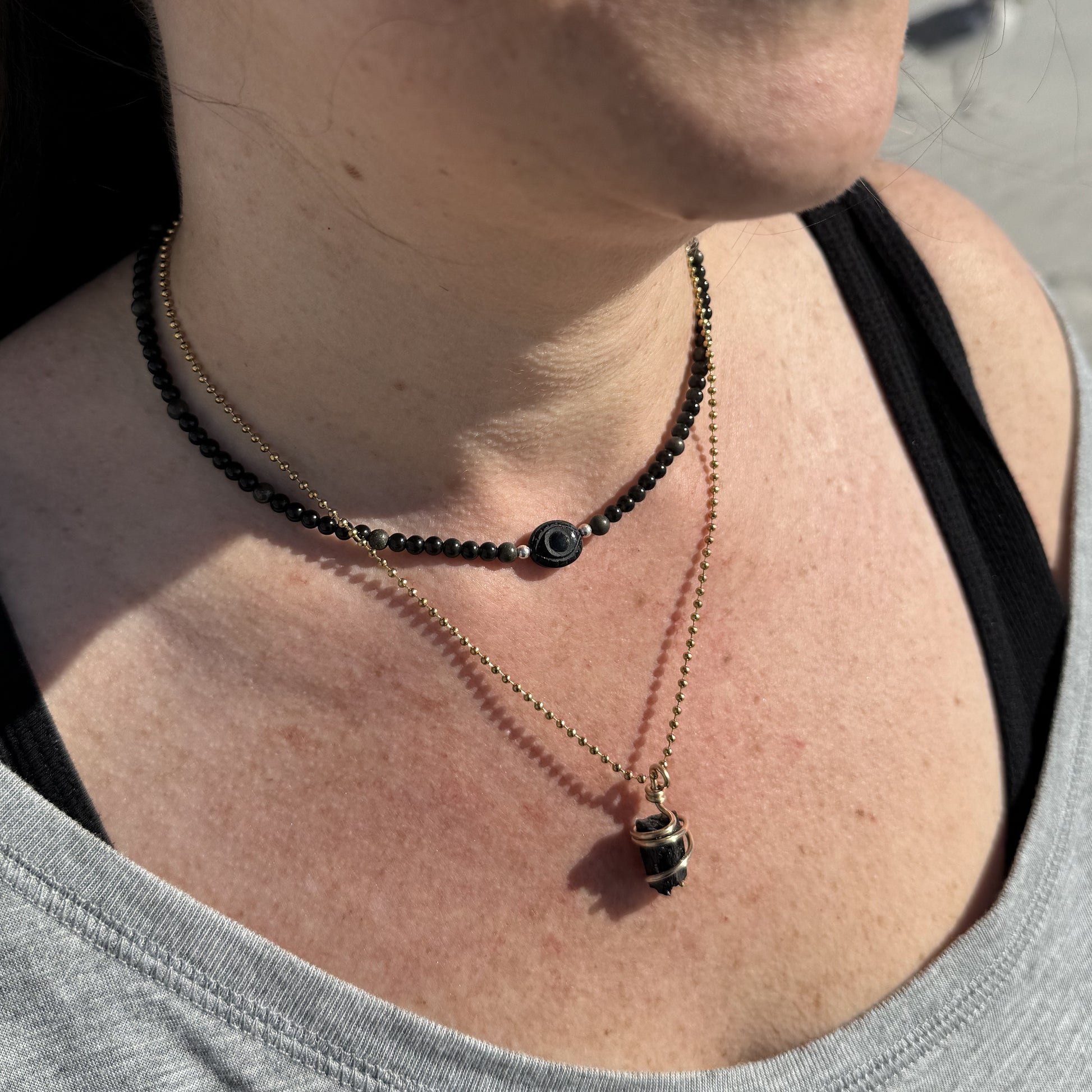 Onyx evil eye necklace layered with obsidian and pyrite beads for protection and balance.