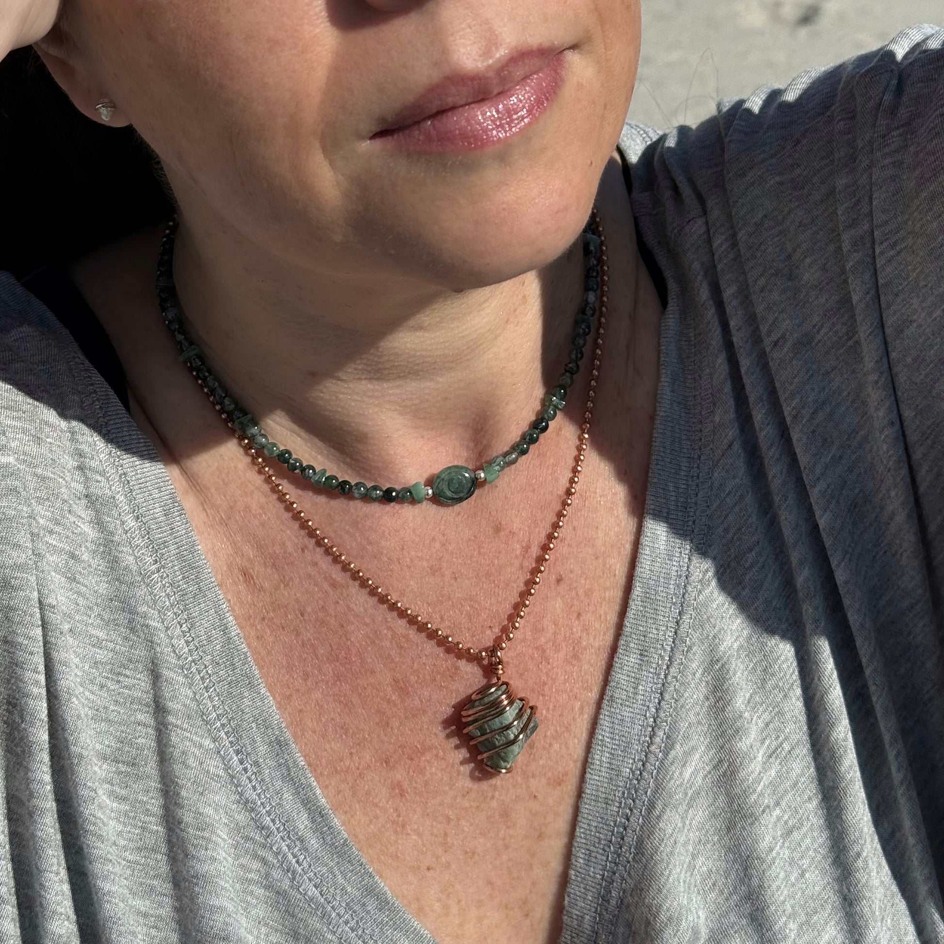 Emerald Evil Eye necklace worn by a woman, featuring green moss agate and emerald beads for heart healing.