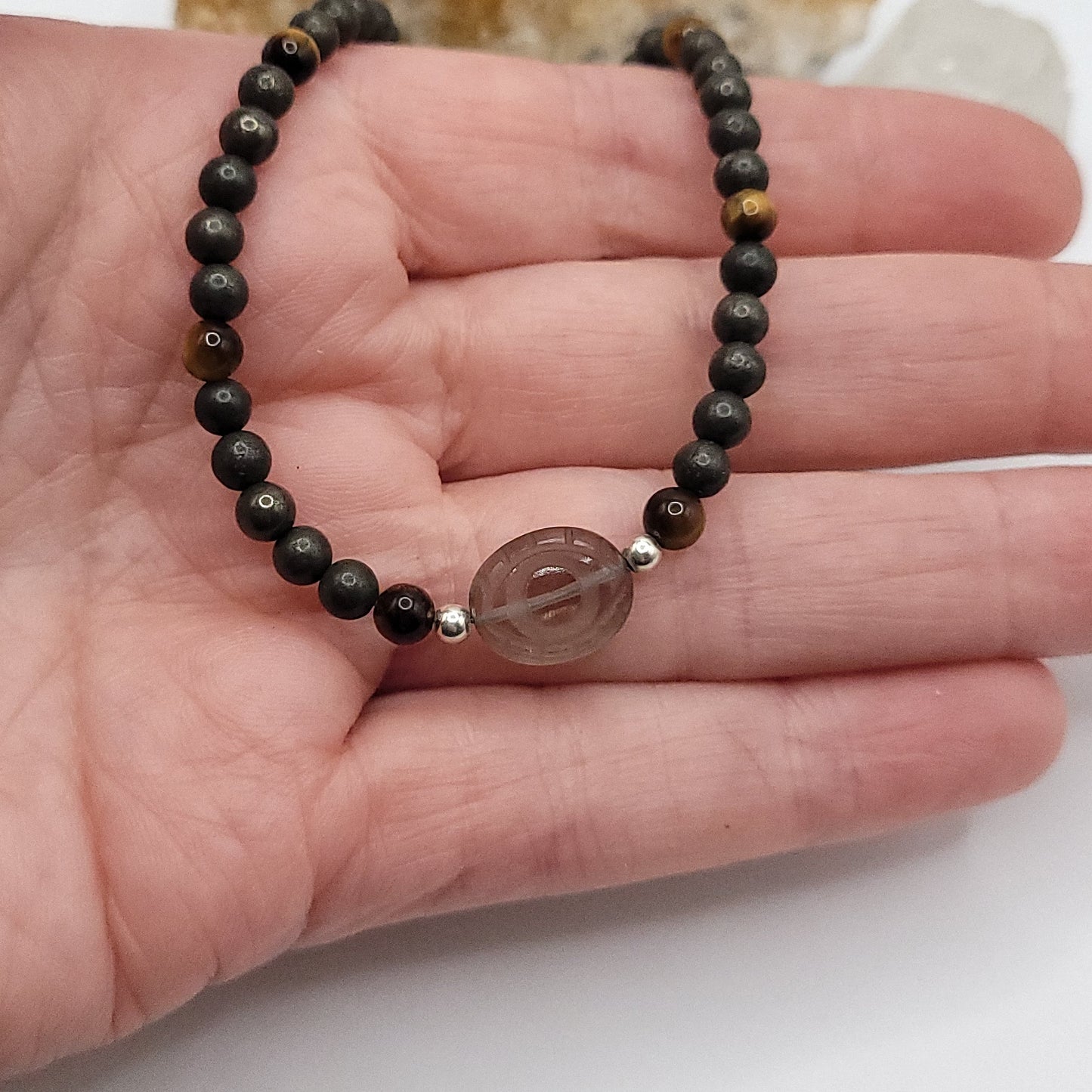 Smoky Quartz Evil Eye necklace shown on hand, featuring Pyrite and Tiger’s Eye beads for grounded confidence.