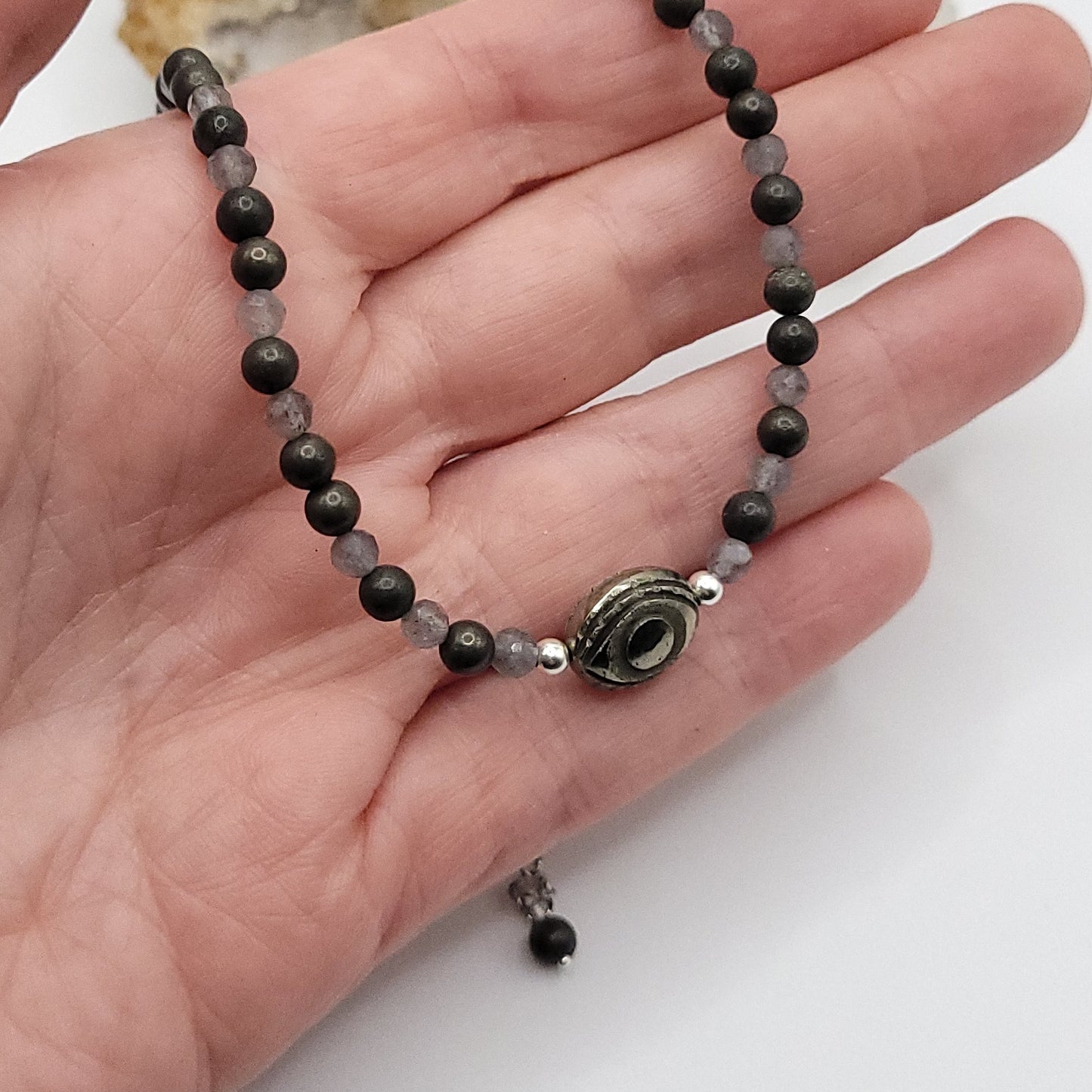Pyrite Evil Eye Necklace displayed in a hand with Pyrite and Labradorite beads for protective strength.