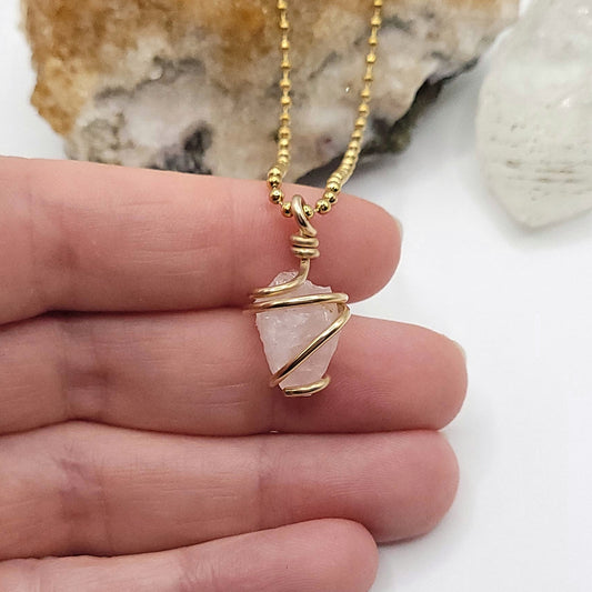 Raw Rose Quartz Necklace in Gold showing a crystal wrapped in 14k gold filled wire on a hand.
