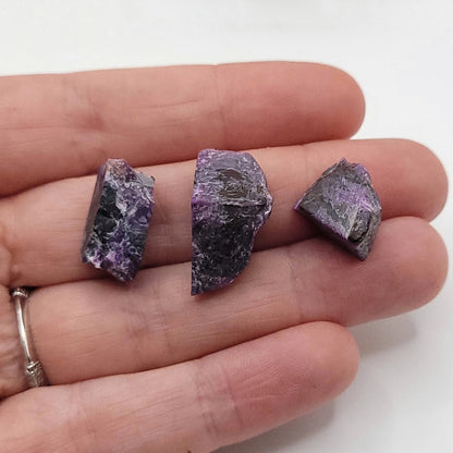 Raw Sugilite necklace stone pieces held in hand, showcasing their unique purple and black colors.