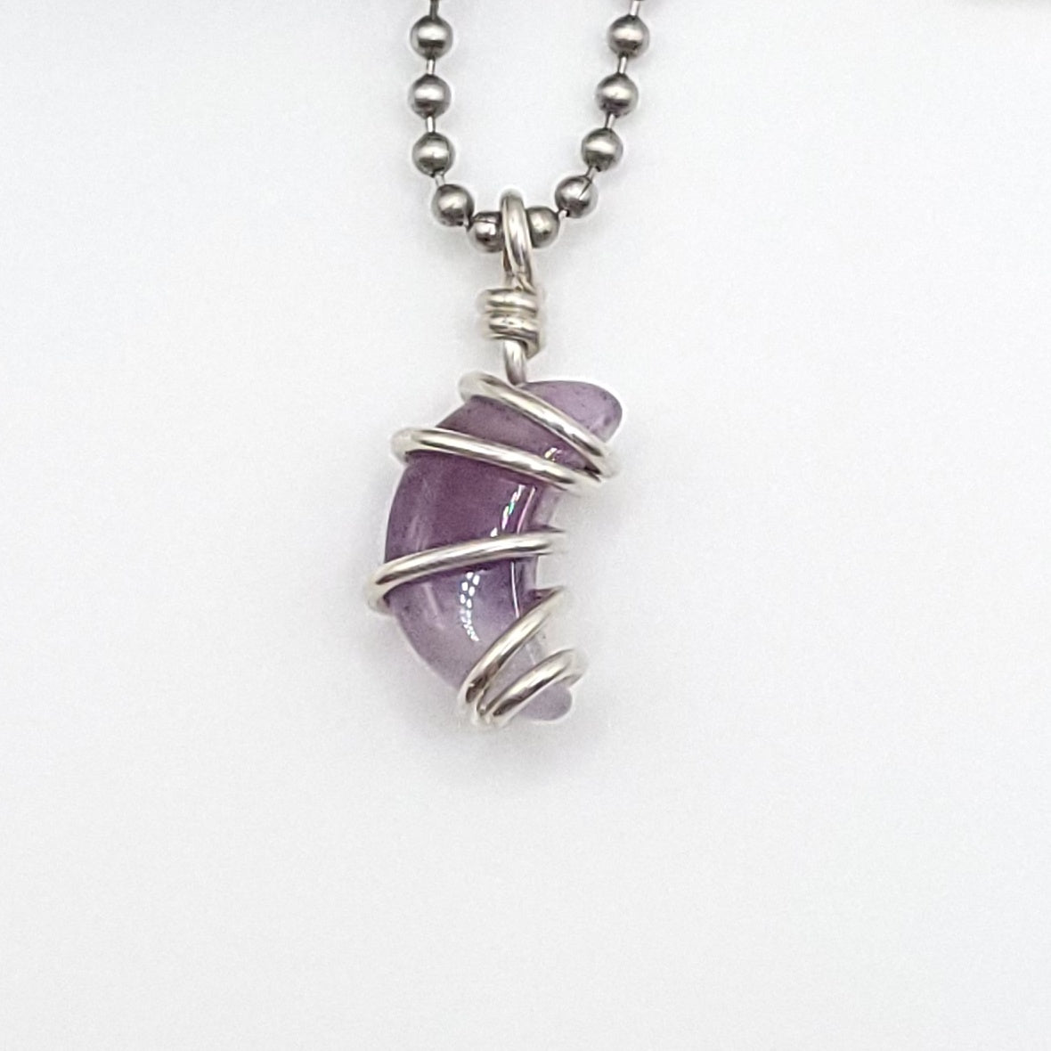 Handmade silver wire‑wrapped purple crystal pendant on a silver bead chain, shown against a white background.