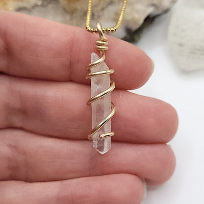 clear quartz necklace in gold close up in hand