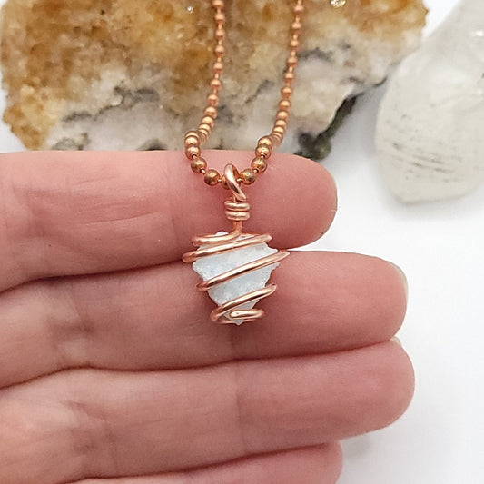 Hand holding a raw blue aragonite necklace wrapped in copper wire, a crystal for inner peace.